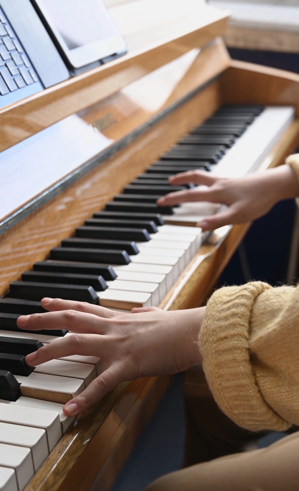 A learner’s hands playing an upright piano